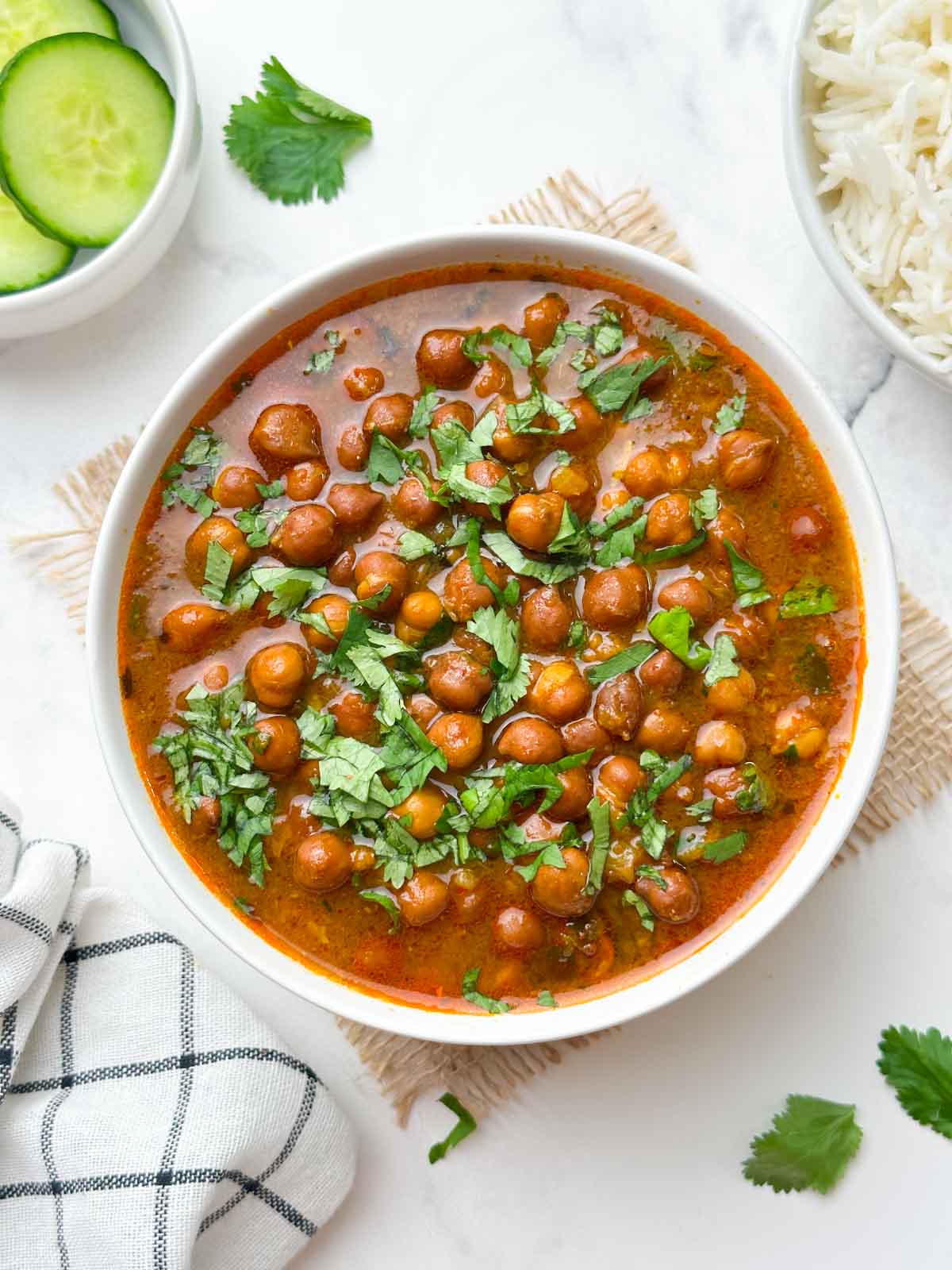 black chickpeas curry (punjabi kala chana) served in a bowl garnish with coriander leaves and spoon in the bowl with cucumber and jeera rice on the side