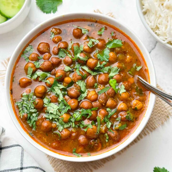 black chickpeas curry (punjabi kala chana) served in a bowl garnish with coriander leaves and spoon in the bowl with cucumber and jeera rice on the side