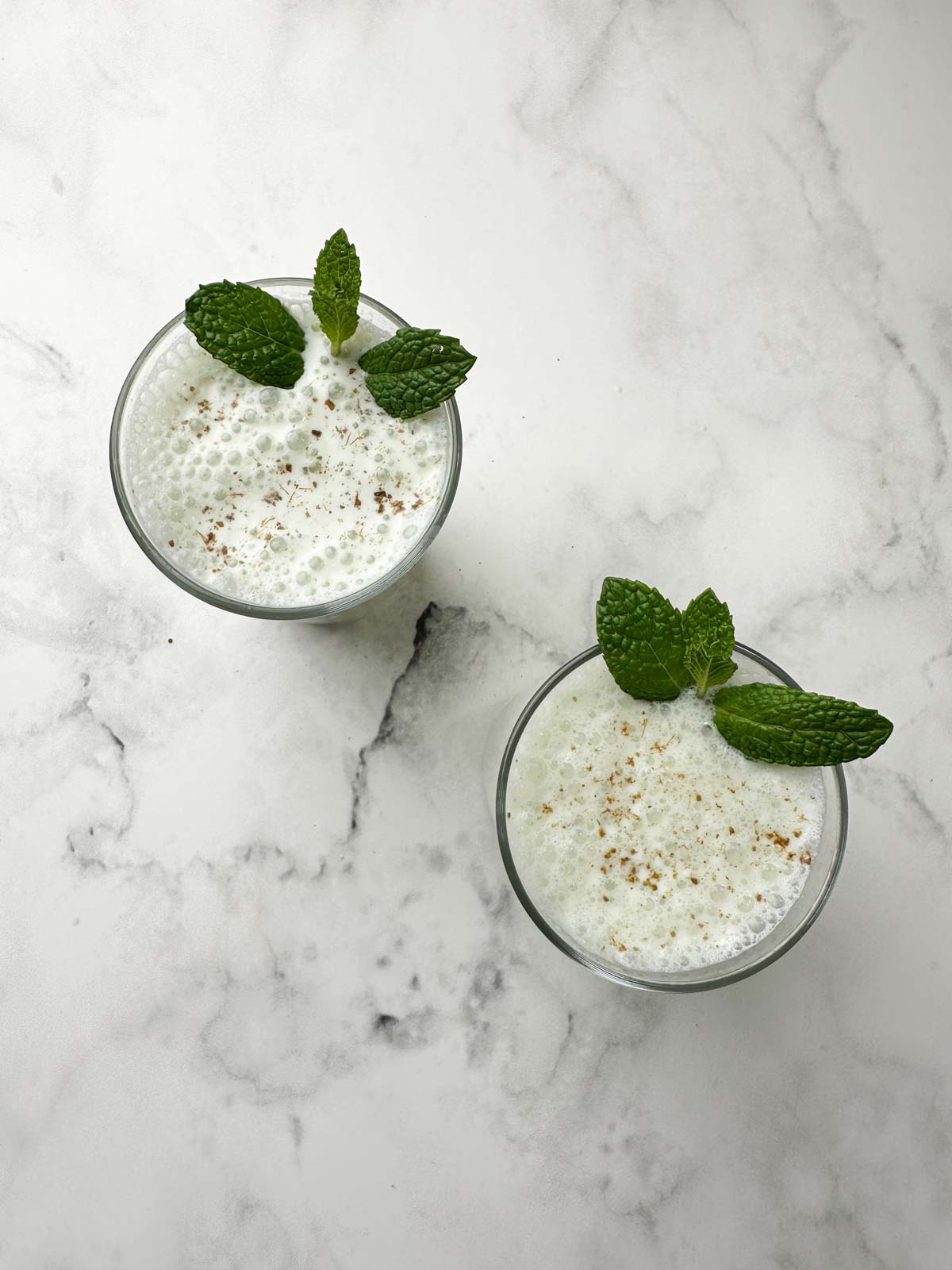 masala chaas (indian spiced buttermilk) served in 2 serving glasses garnished with mint leaves and roasted cumin powder