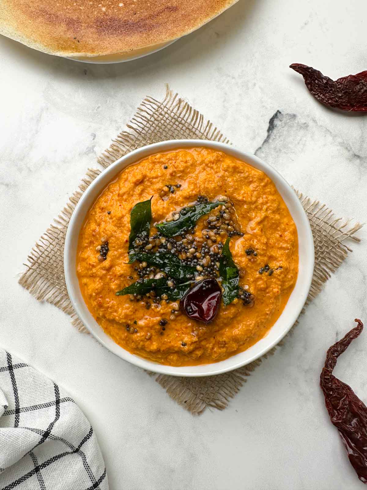 red coconut chutney served in a white bowl with tempering on the top and dosa on the side