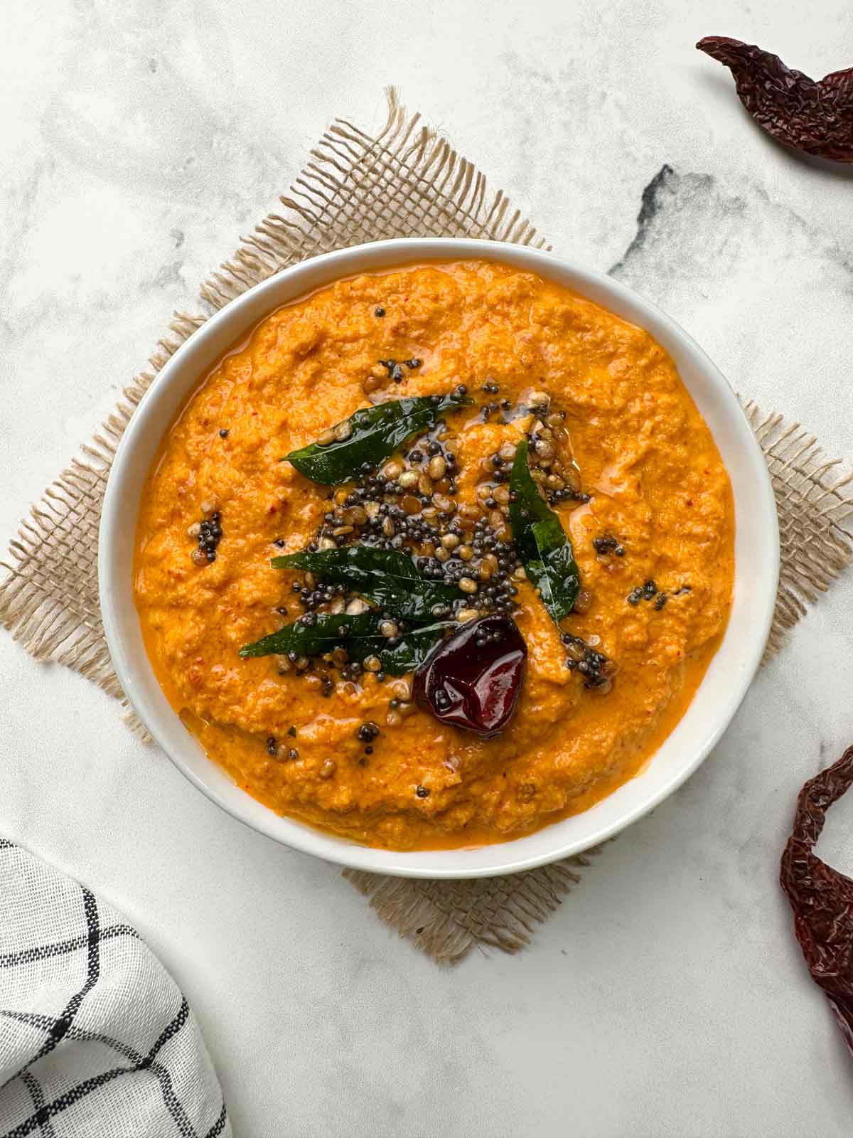 red coconut chutney served in a white bowl with tempering on the top