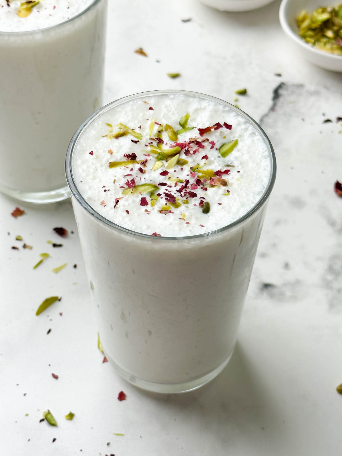 two glass of sweet lassi served in serving glasses garnished with pistachios and dried rose petals
