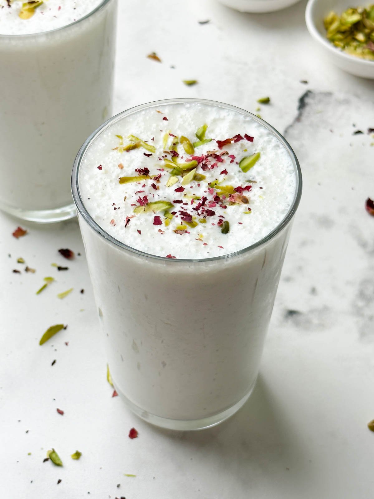 two glass of sweet lassi served in serving glasses garnished with pistachios and dried rose petals