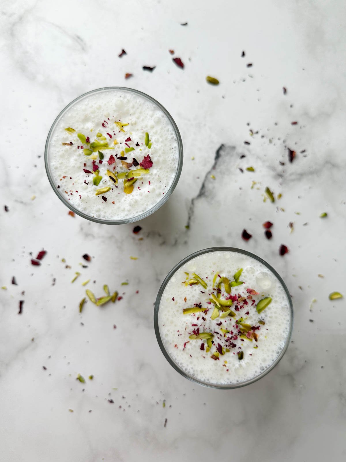 two glass of sweet lassi served in serving glasses garnished with pistachios and dried rose petals