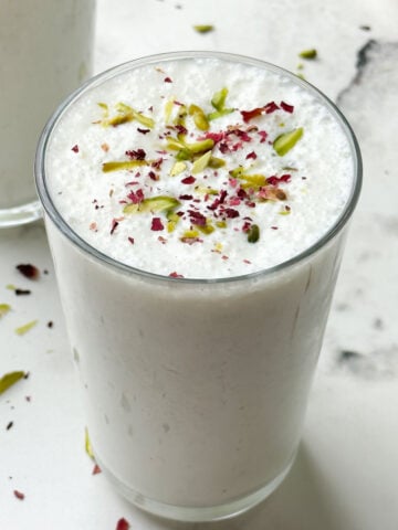 two glass of sweet lassi served in serving glasses garnished with pistachios and dried rose petals