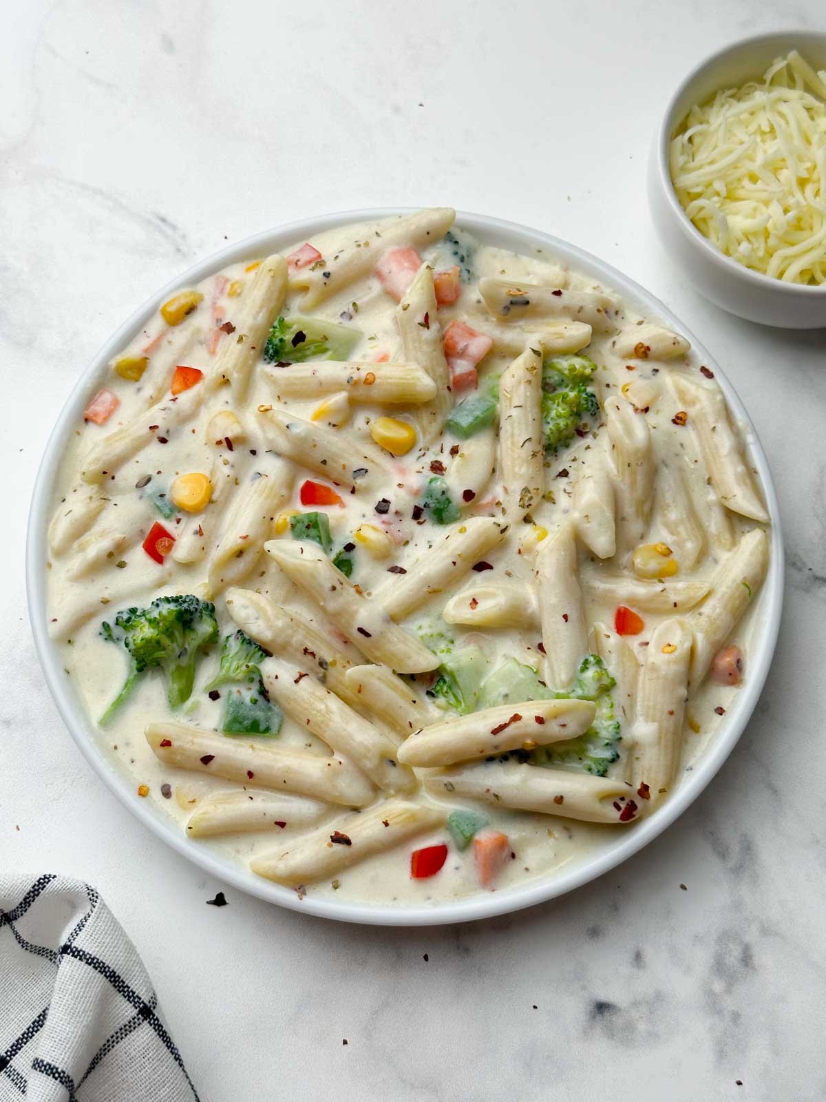 white sauce pasta (bechamel sauce pasta) served in a plate with cheese on the side