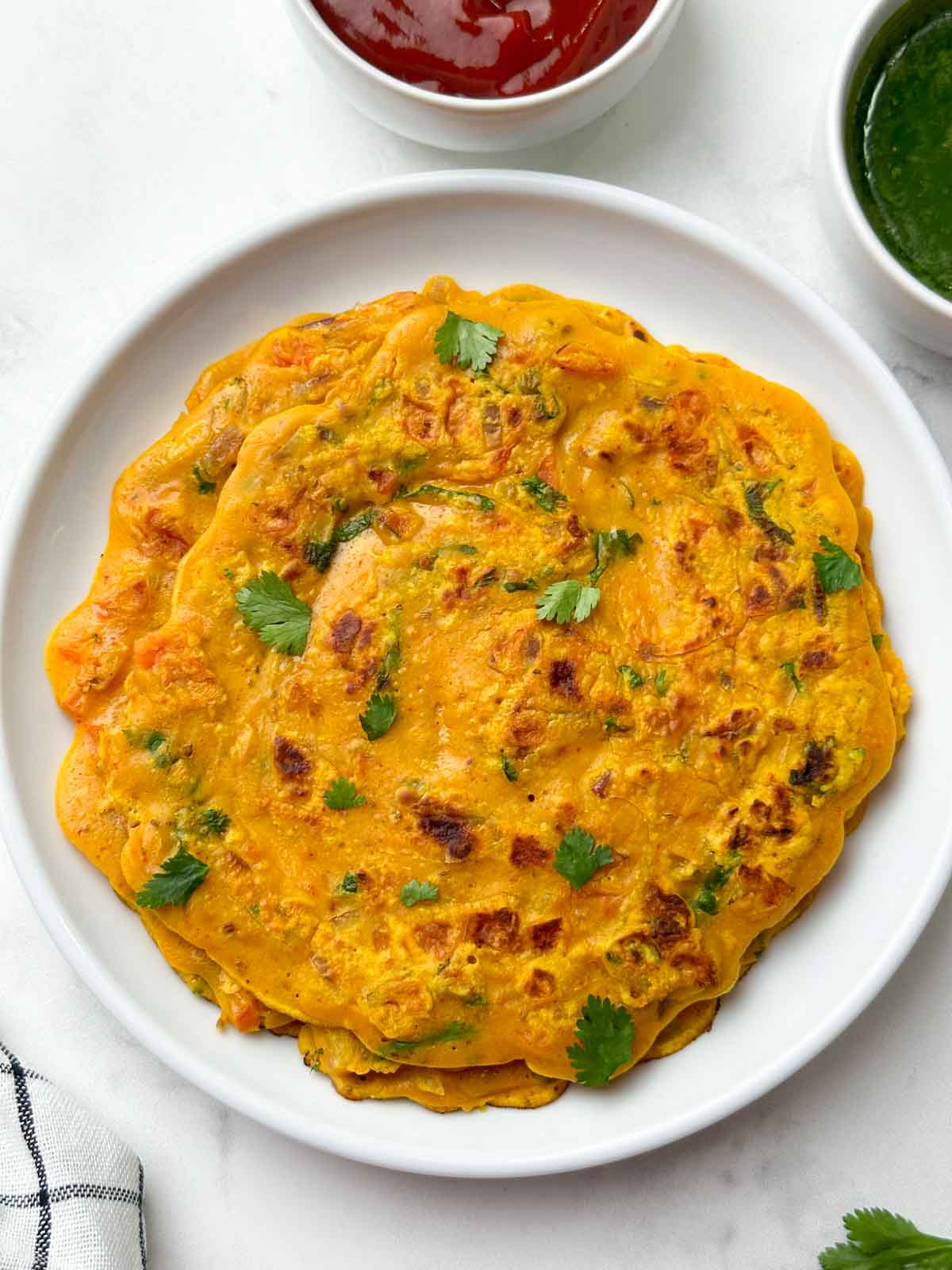 gram flour pancake served on a white plate with green chutney on the side