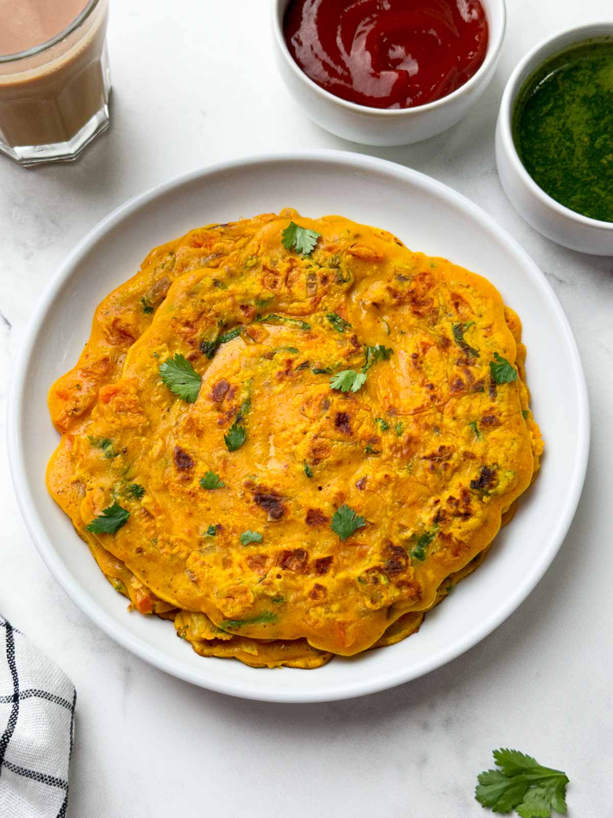 besan chilla served on a plate with chutneys on the side and masala tea on the side