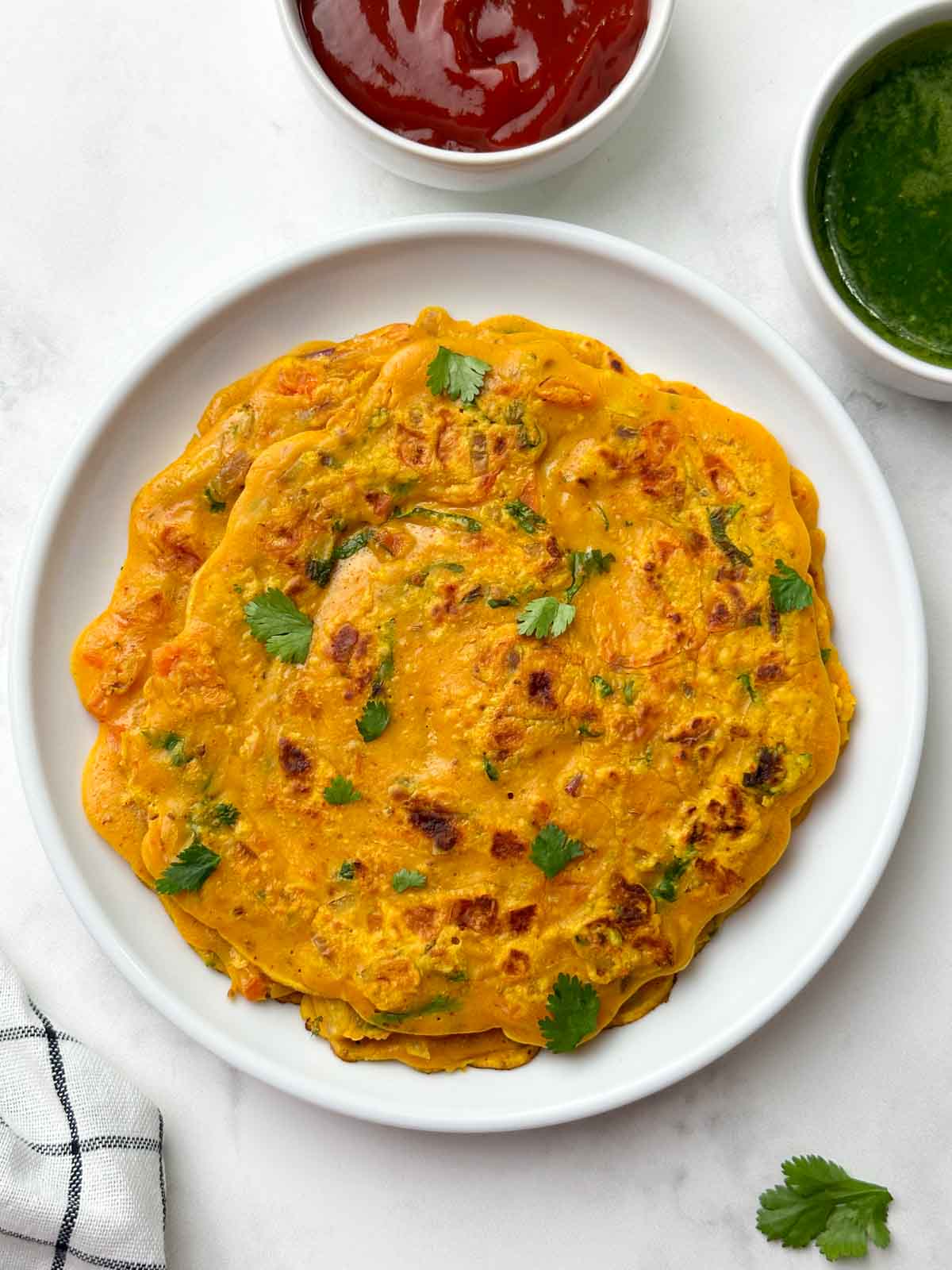 besan chilla served on a white plate with green chutney on the side