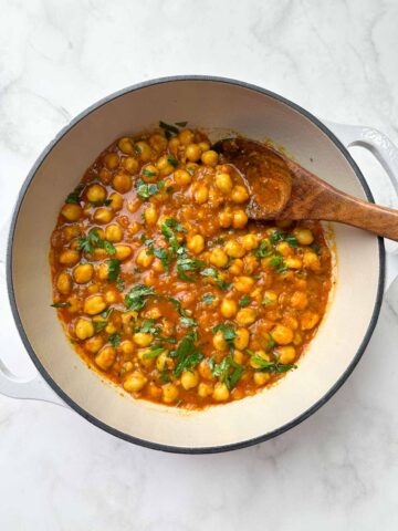 chana masala curry in a dutch oven with a wooden spoon