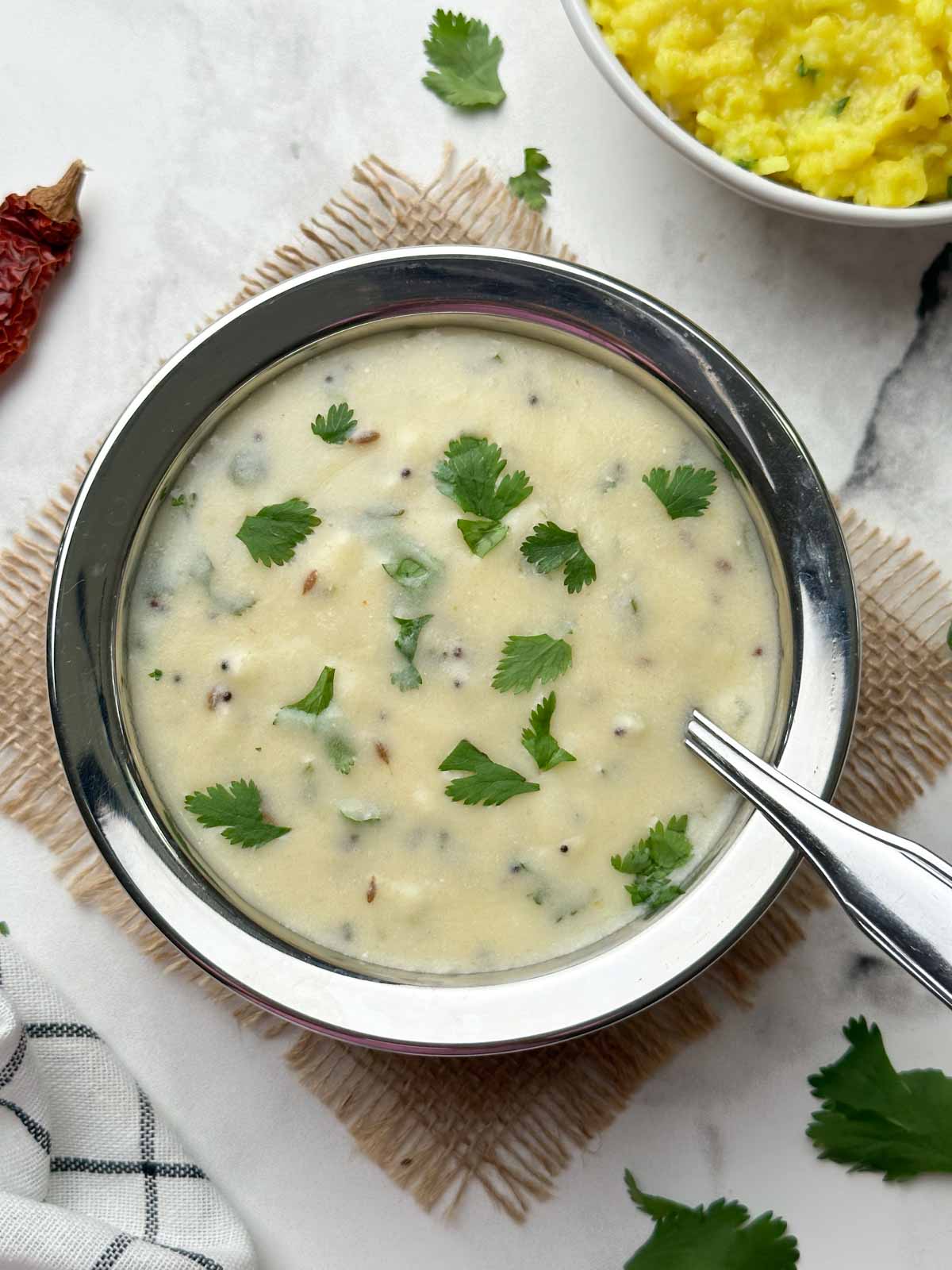 gujarati kadhi served in a bowl with a spoon and khichdi on the side