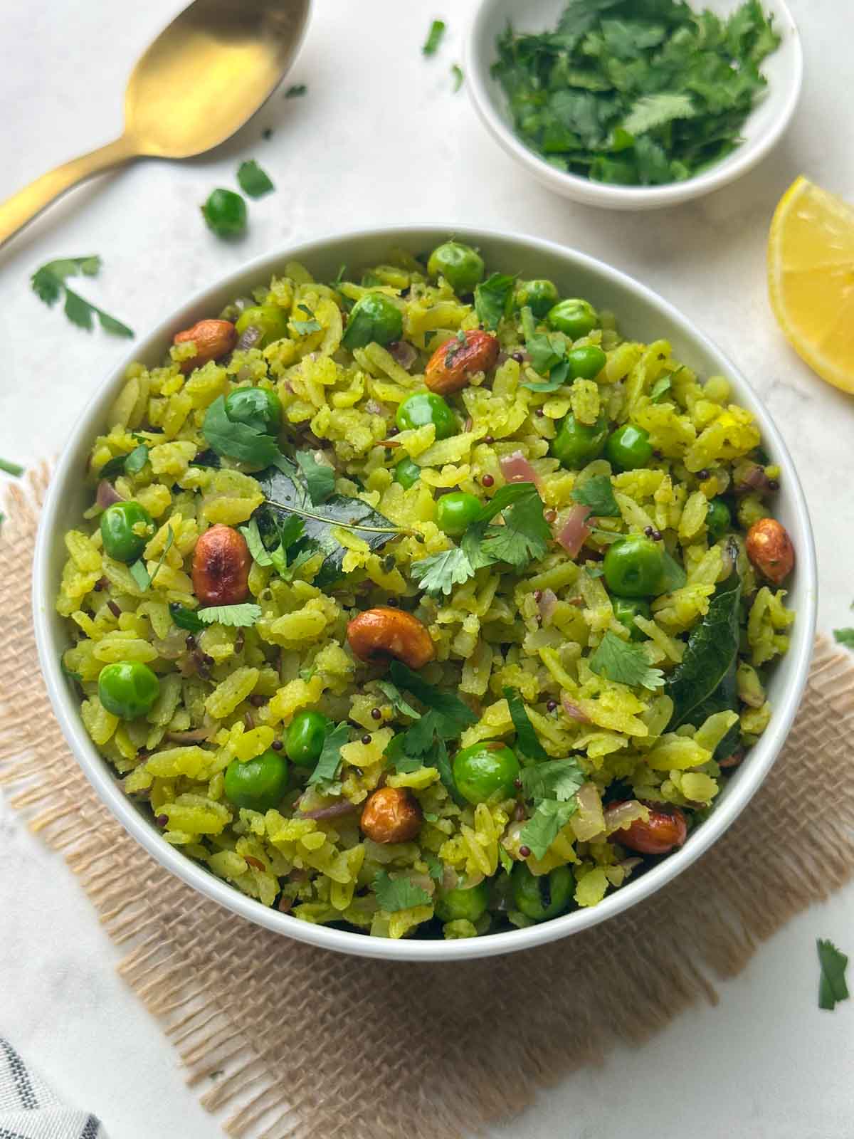 green chutney poha (hariyali poha) served in a bowl with coriander leaves and lemon wedge on the side