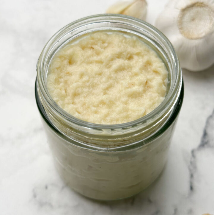 homemade fresh garlic paste in a glass container with garlic bulb on the side