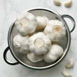 whole garlic bulbs in a mesh container and cloves on the ground