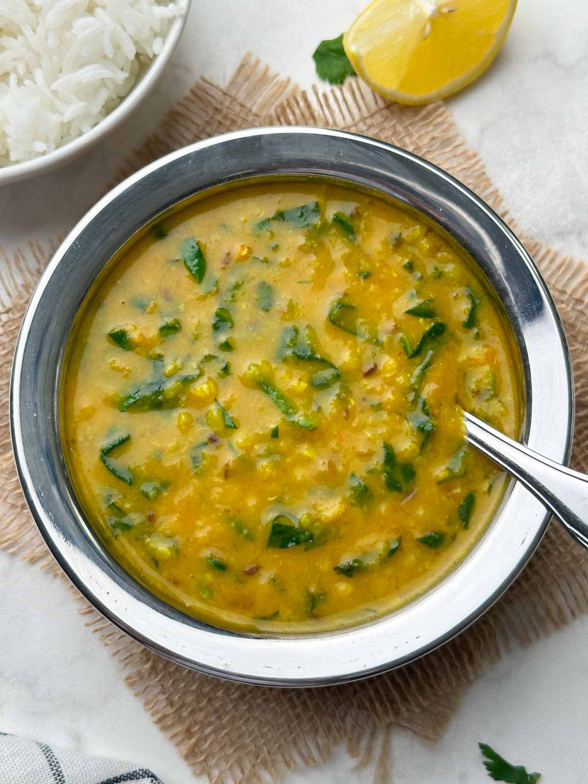 dal palak recipe served in a kadai with a spoon and rice on the side