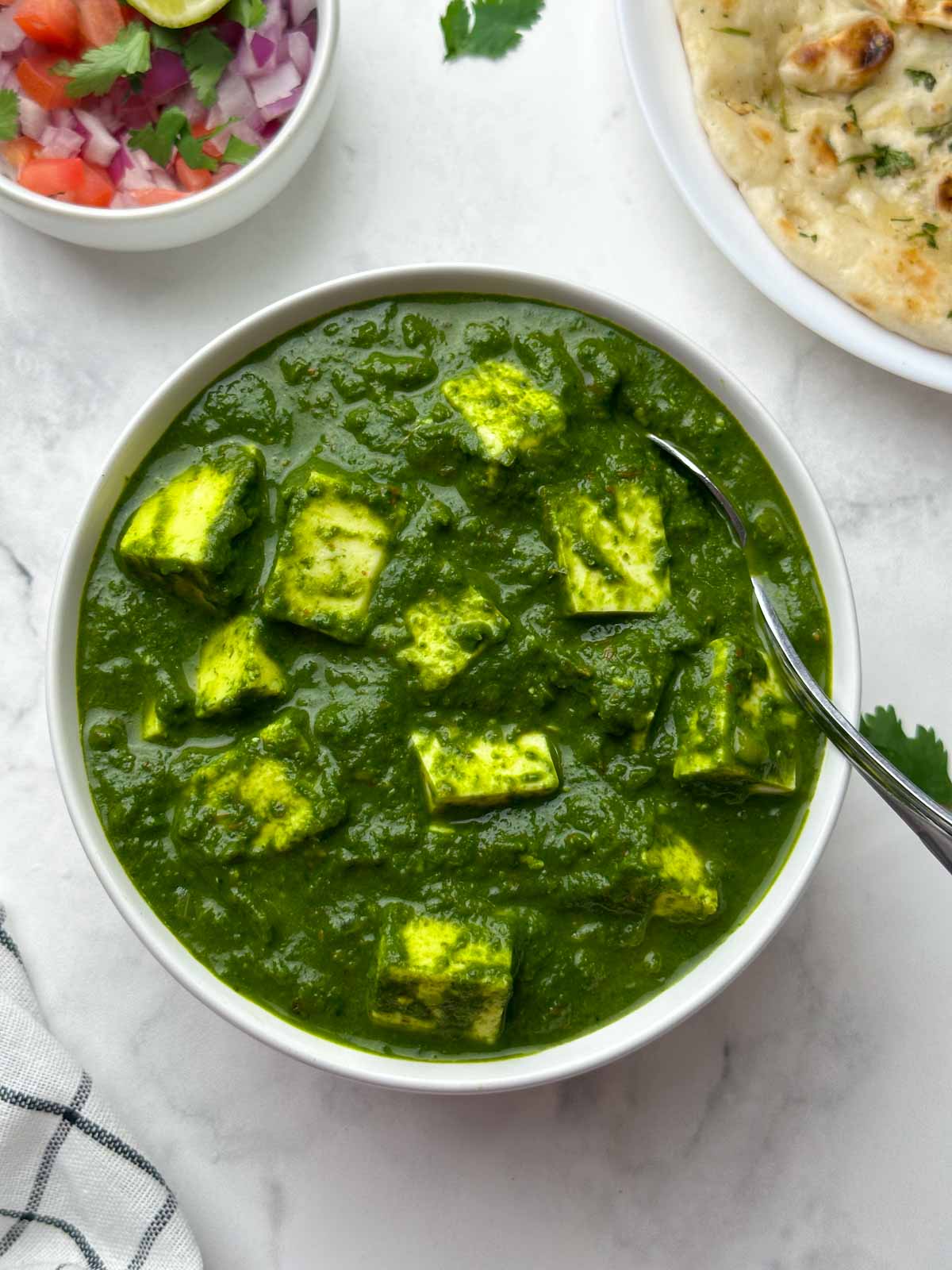 palak paneer served in a white bowl with salad and garlic naan on the side