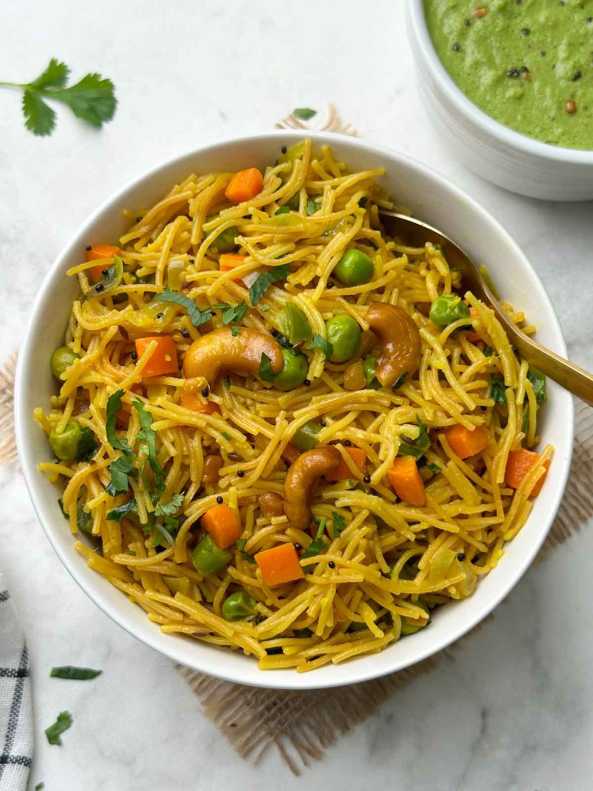 vermicelli/semiya upma served in a white bowl with a spoon and green coconut chutney on the side