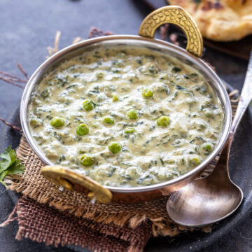 Methi matar malai served in a kadai with a spoon and naan on the side