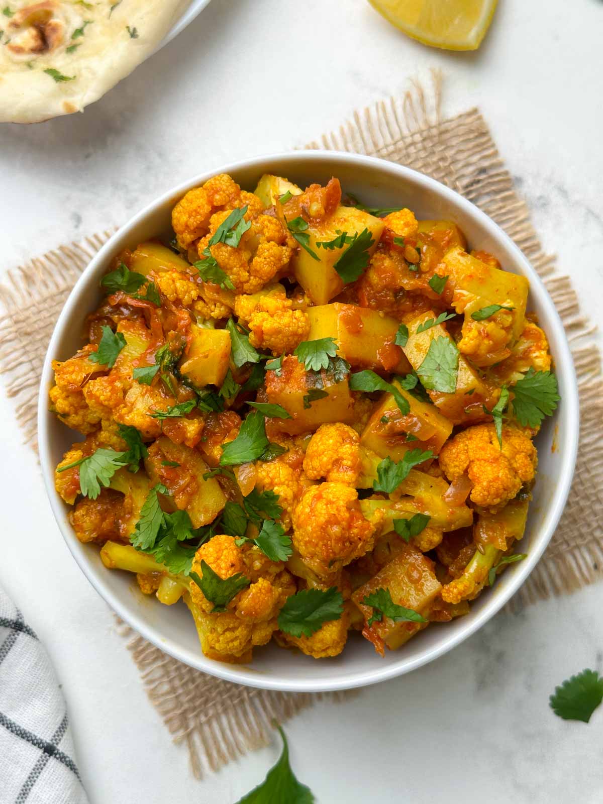 aloo gobi sabzi served in a bowl with garlic naan and lemon wedge on the side