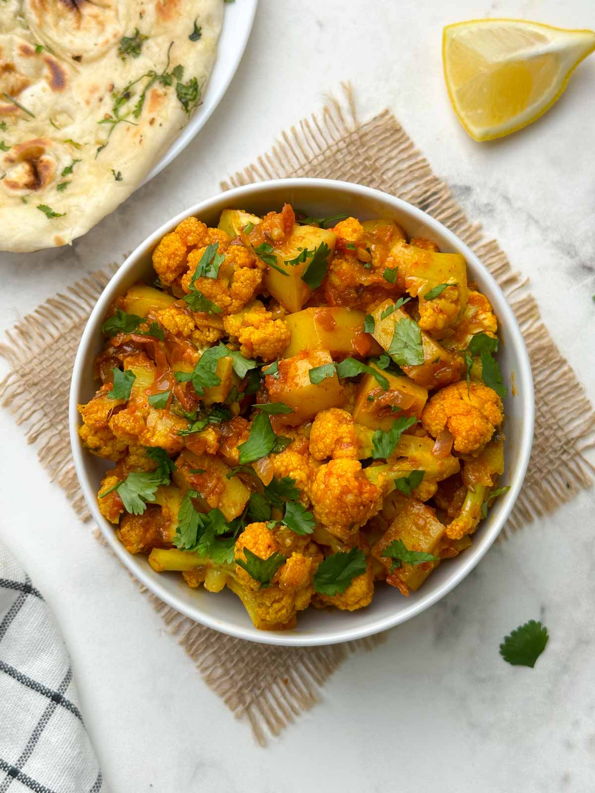 potato cauliflower curry served in a bowl with garlic naan and lemon wedge on the side