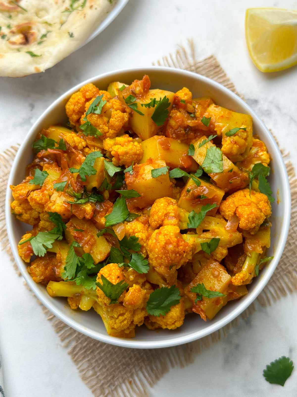 aloo gobi sabzi served in a bowl with garlic naan and lemon wedge on the side