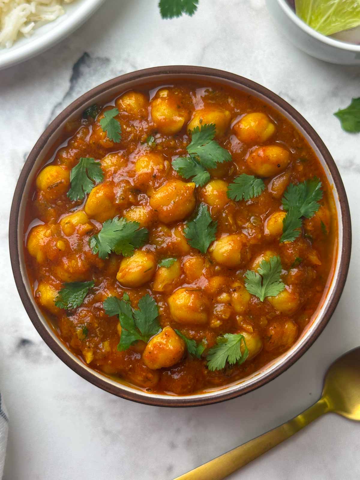 restaurant style chana masala served in a bowl with rice, salad and spoon on the side