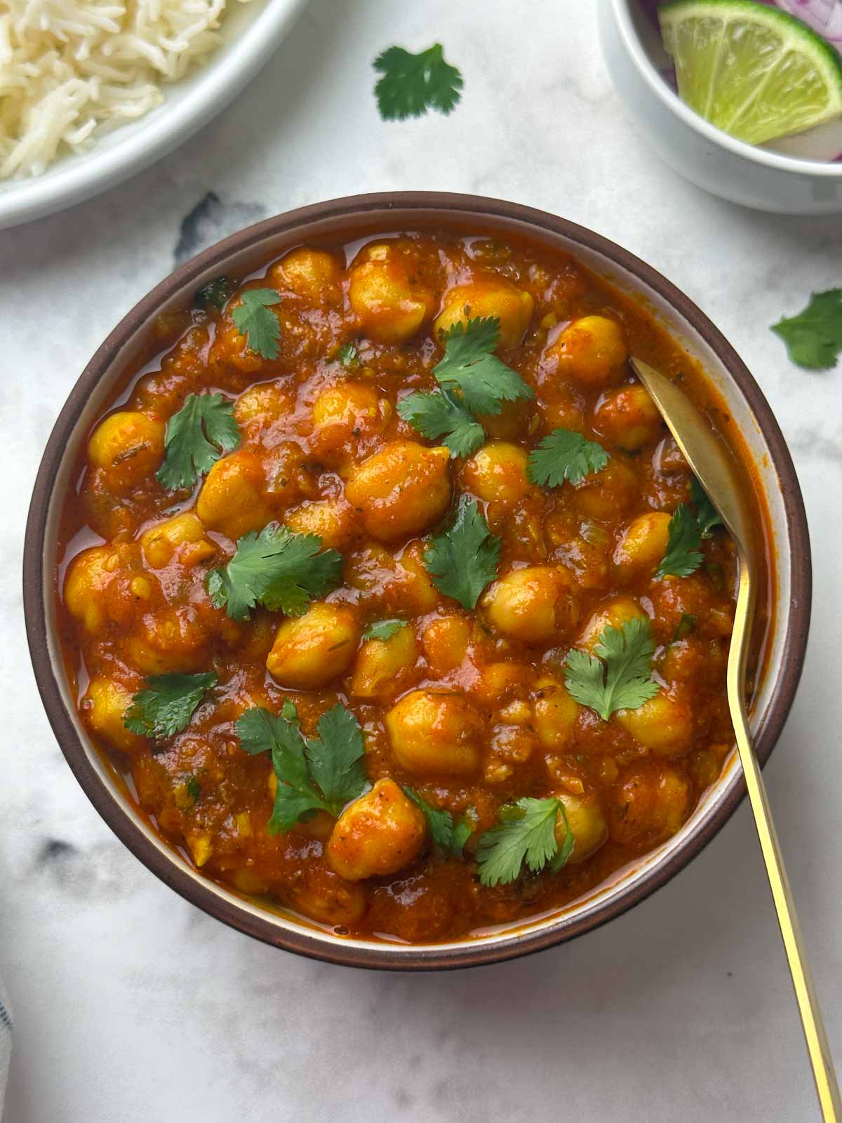 restaurant style chana masala curry served in a bowl with a spoon and rice, and salad on the side