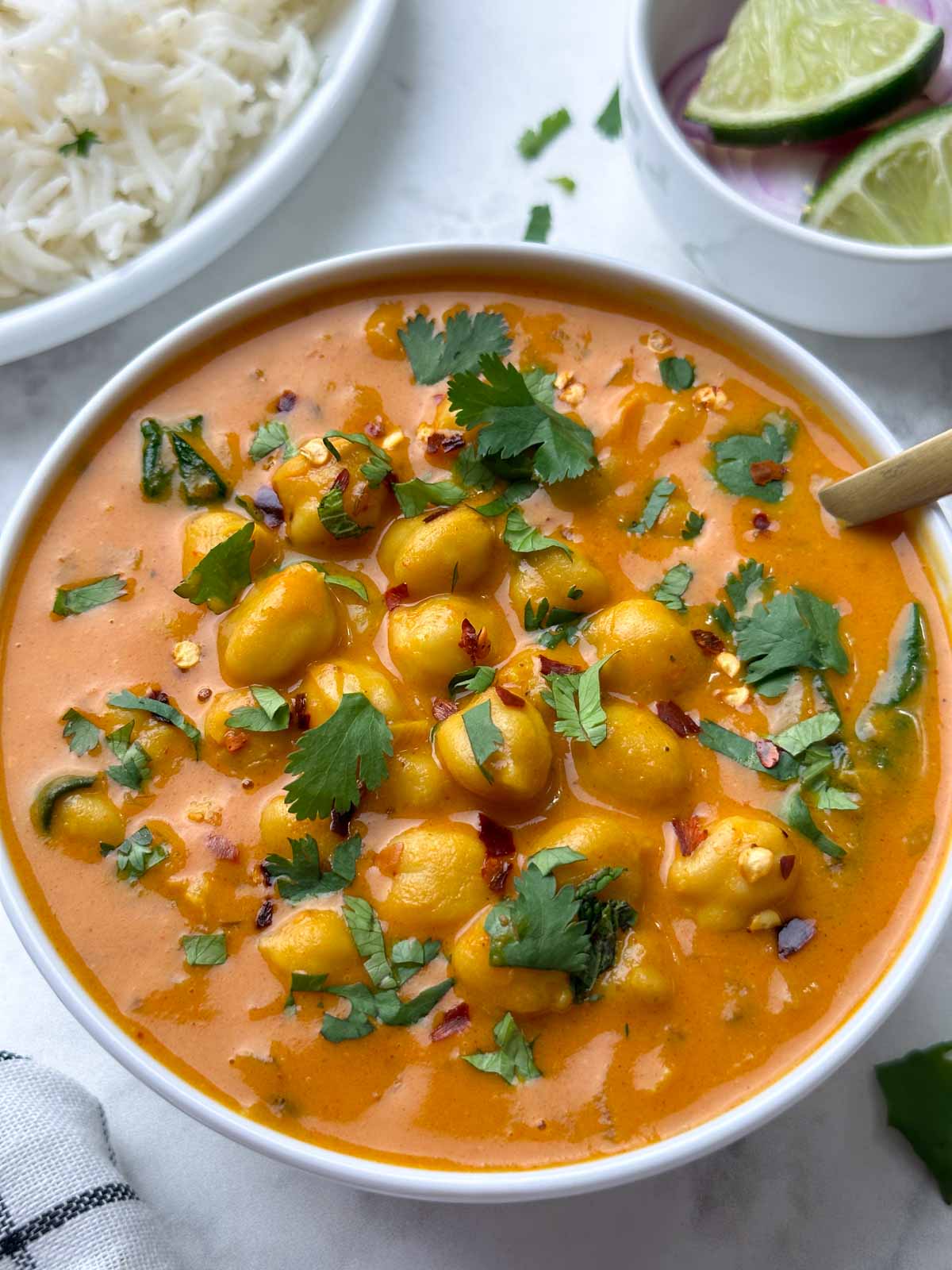 chickpea coconut curry served in a white bowl garnished with coriander leaves and rice and lime edge on the side