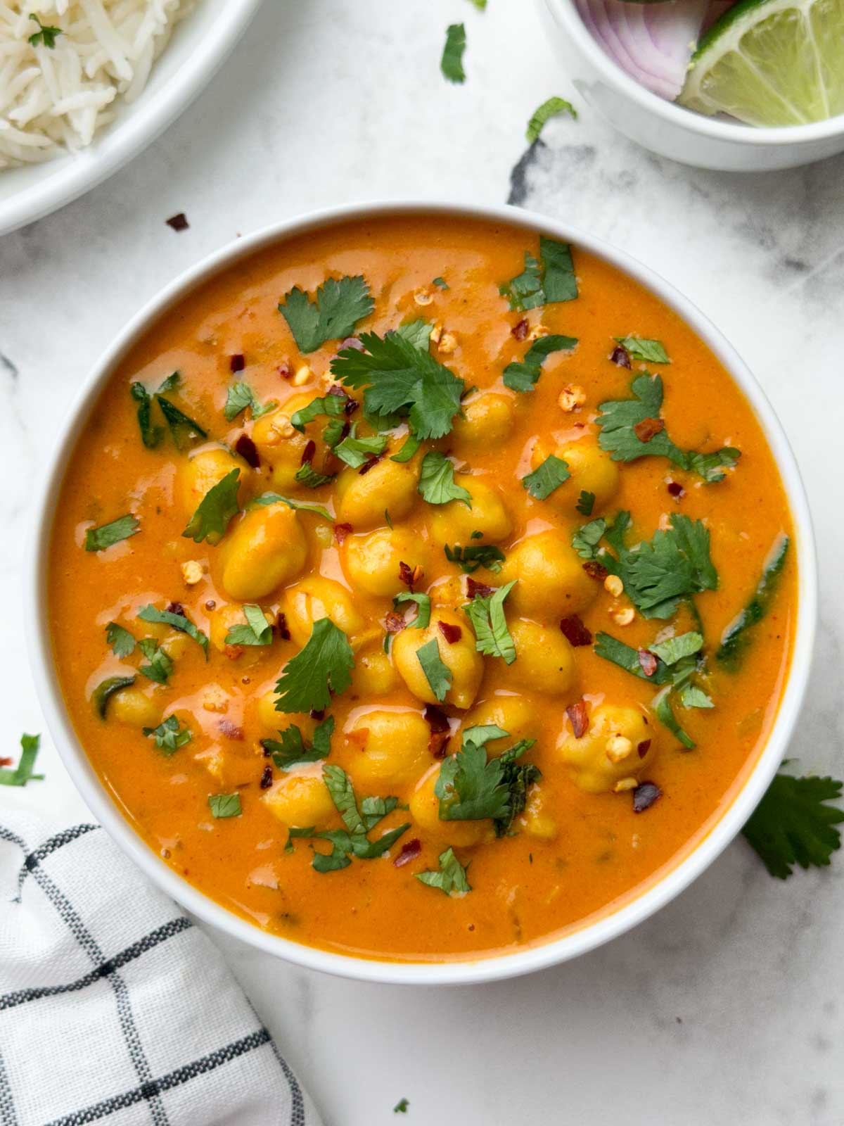 chickpea coconut curry served in a white bowl garnished with coriander leaves and rice and lime edge on the side