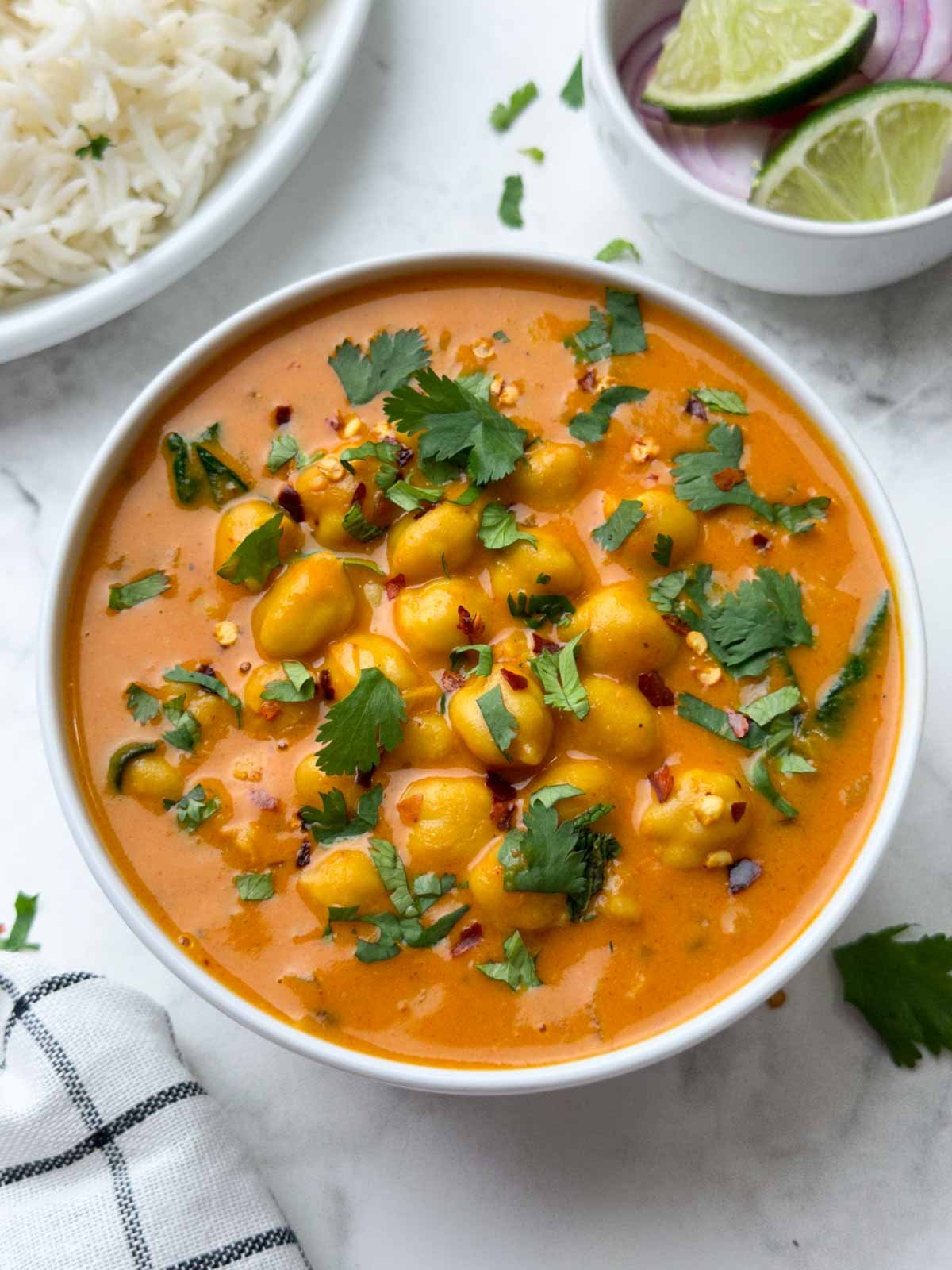 chickpea coconut curry served in a white bowl garnished with coriander leaves and rice and lime edge on the side