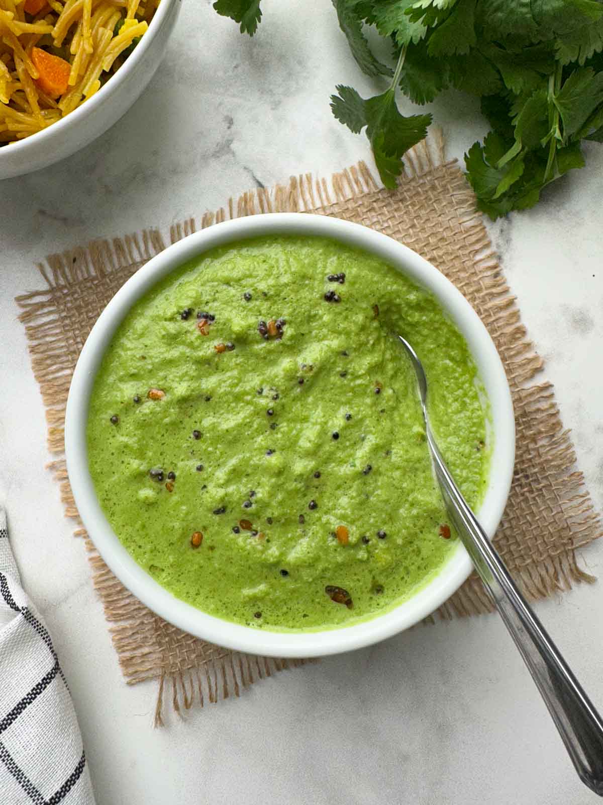 coriander coconut chutney served in a bowl with a spoon and vermicelli upma and coriander leaves on the side