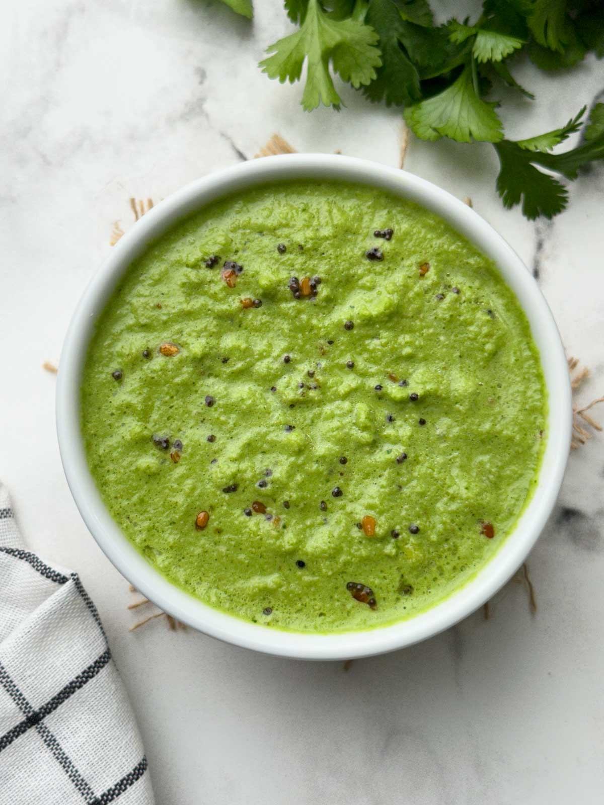 green coriander coconut chutney served in a bowl and coriander leaves on the side