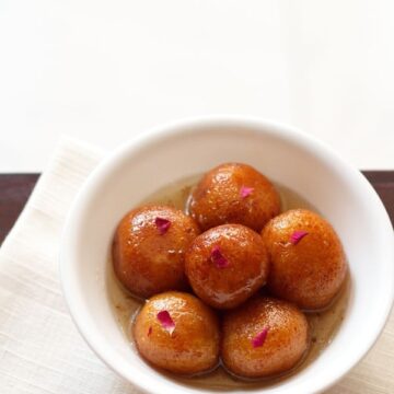 gulab jamun served in a bowl garnished with rose petals.