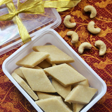 kaju katli in a plastic box with raw cashews on the side