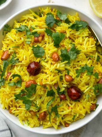 indian lemon rice served in a bowl with a spoon and lemon wedge and coriander leaves on the side