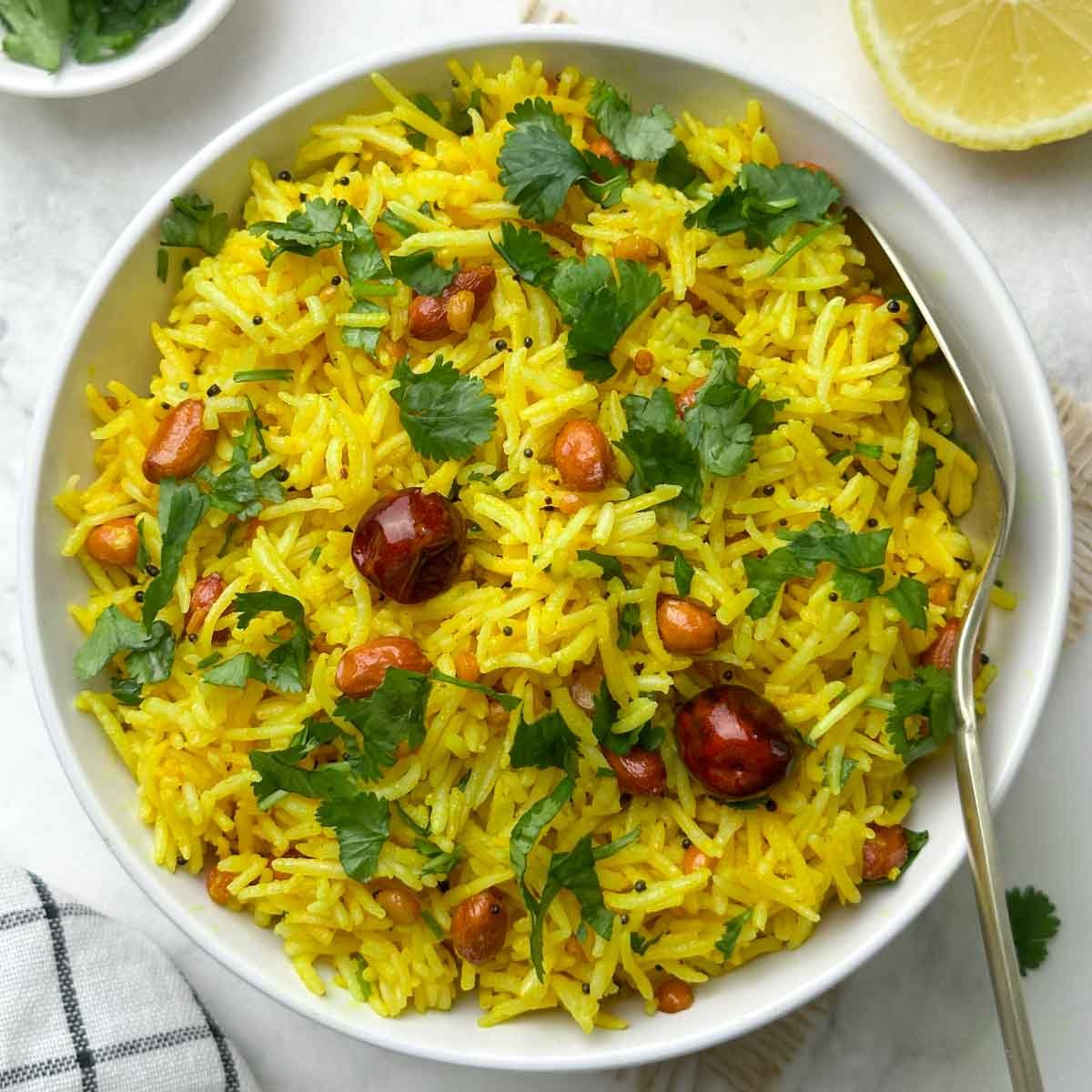 indian lemon rice served in a bowl with a spoon and lemon wedge and coriander leaves on the side