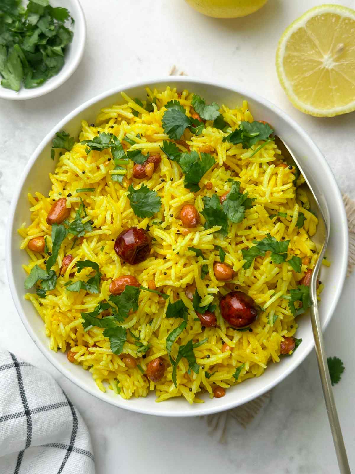 indian lemon rice served in a bowl with a spoon and lemon wedge and coriander leaves on the side