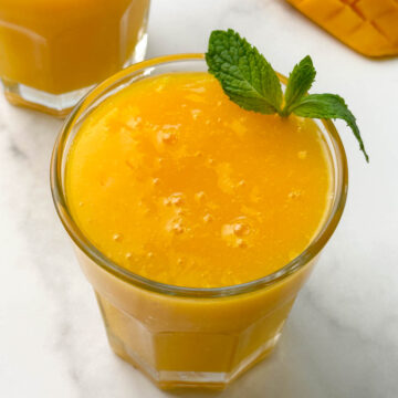 mango juice served in 2 glass containers with mint on the top for garnishing
