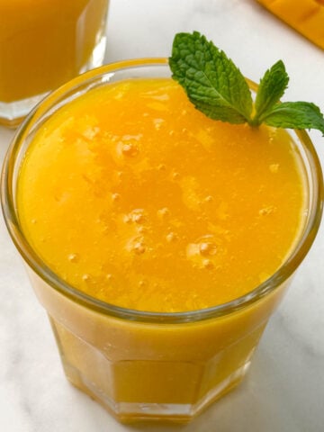 mango juice served in 2 glass containers with mint on the top for garnishing