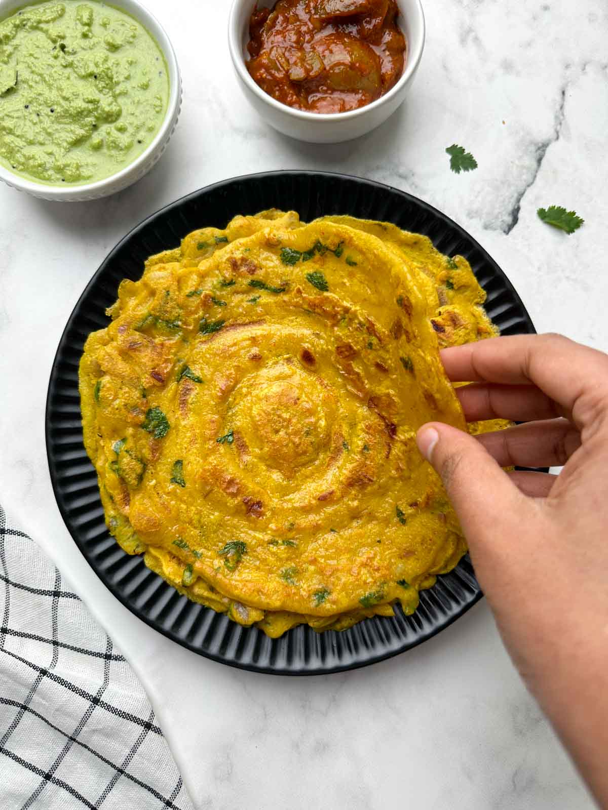 holding cheela in hand with coriander chutney and pickle on the side