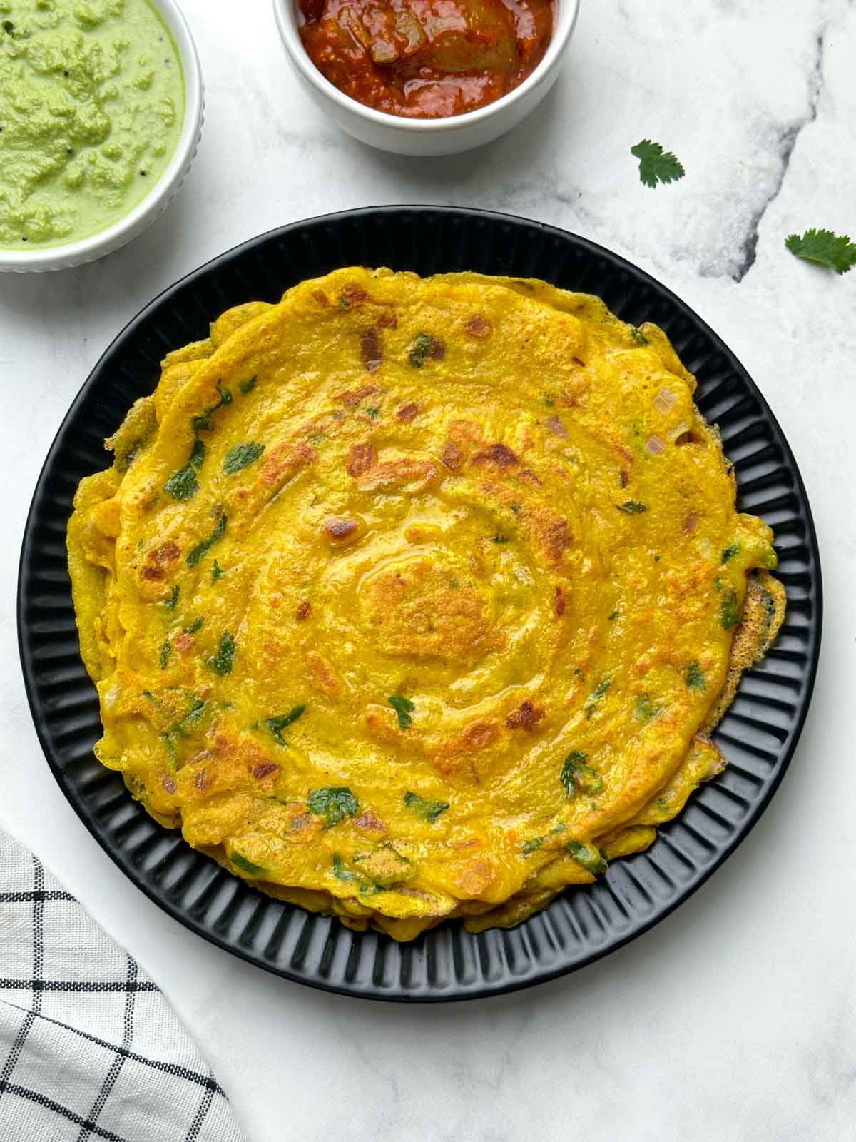 moong dal chilla stacked on a plate with pickle and coconut chutney on the side