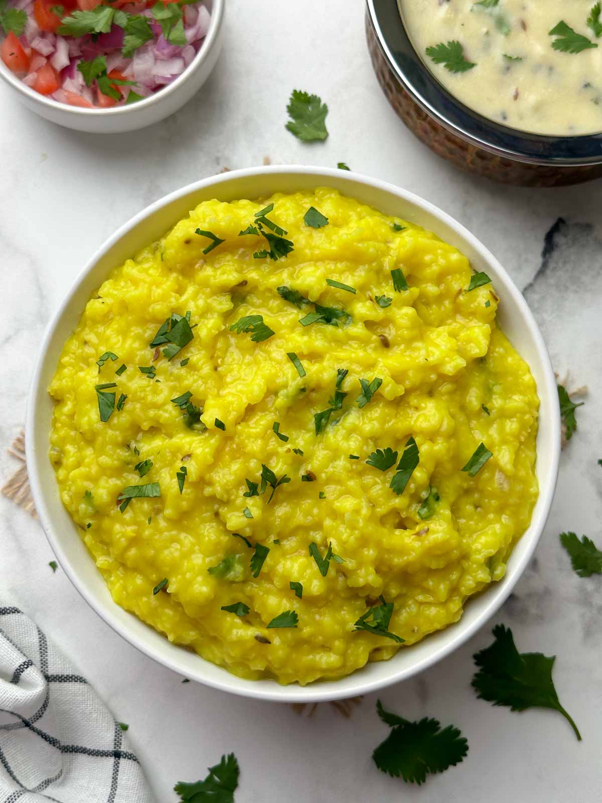 khichdi served in a bowl garnished with cilantro with kadhi on the side