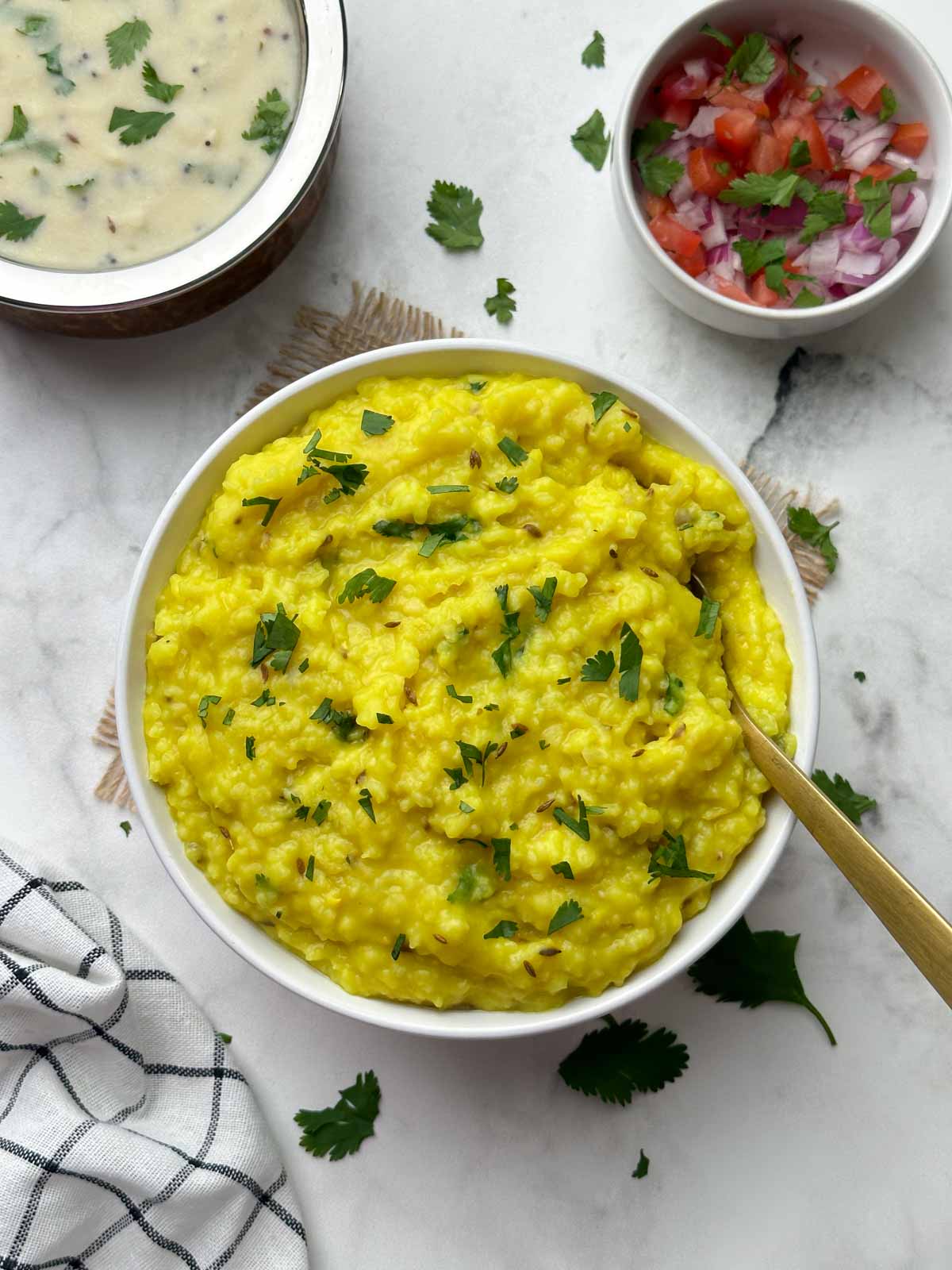 moong dal khichdi served in a bowl with a spoon and kadhi and salad on the side