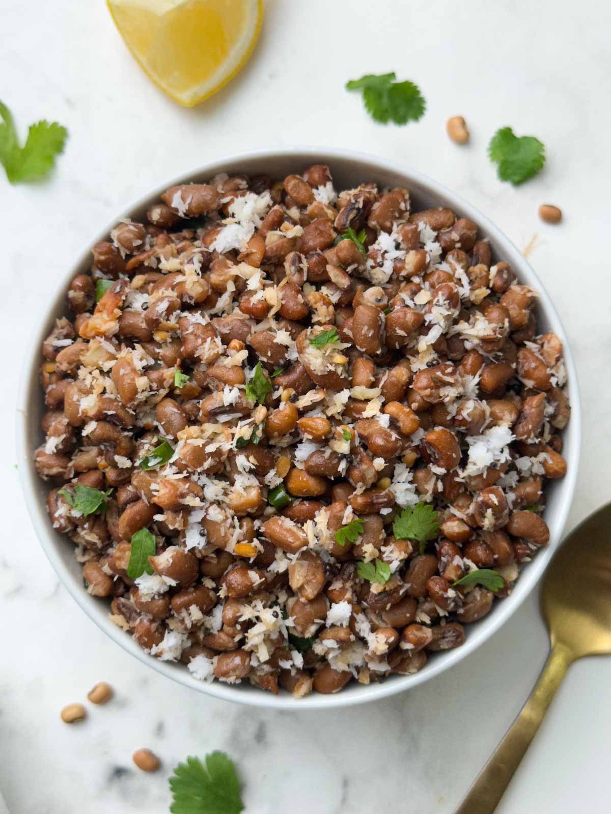 red chori sundal (beans sundal) served in a white bowl garnished with cilantro with a spoon and lemon wedge on the side