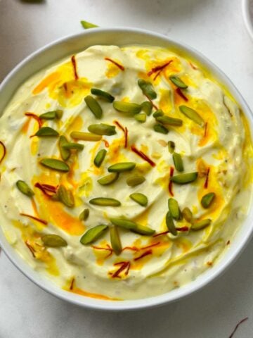 shrikhand served in a bowl with poori, pista and saffron strands on the side