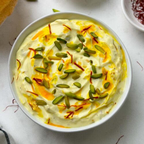 shrikhand served in a bowl with poori, pista and saffron strands on the side