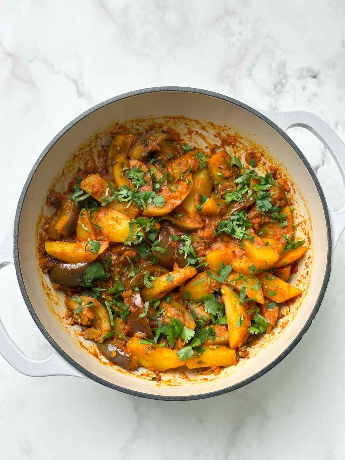 potato eggplant curry in a dutch oven garnished with coriander leaves