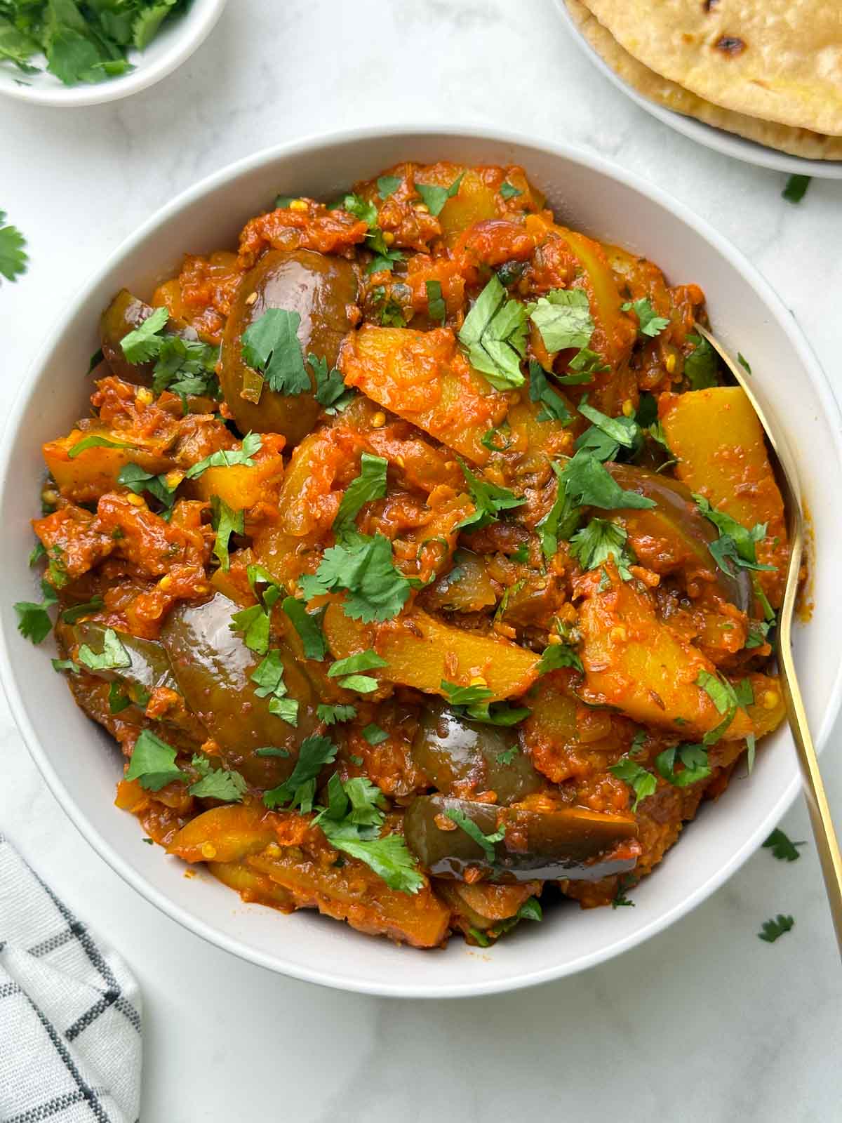 aloo baingan served in a bowl with a spoon with roti and coriander leaves on the side