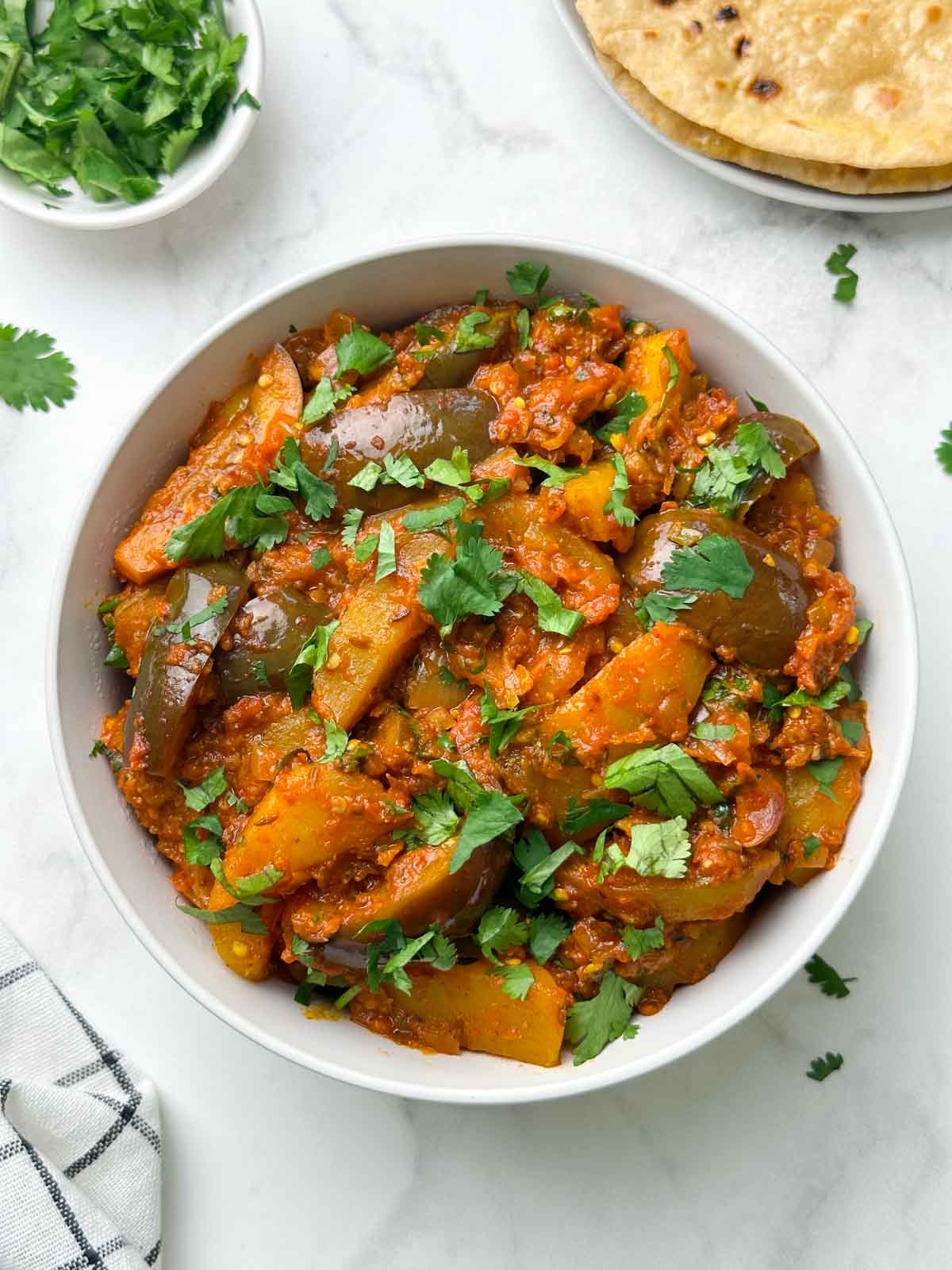 aloo baingan served in a bowl with roti and coriander leaves on the side