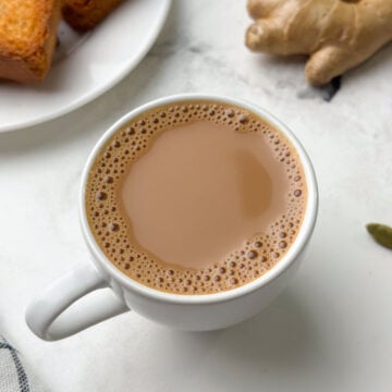 ginger tea served in a cup with rusk and ginger knob on the side